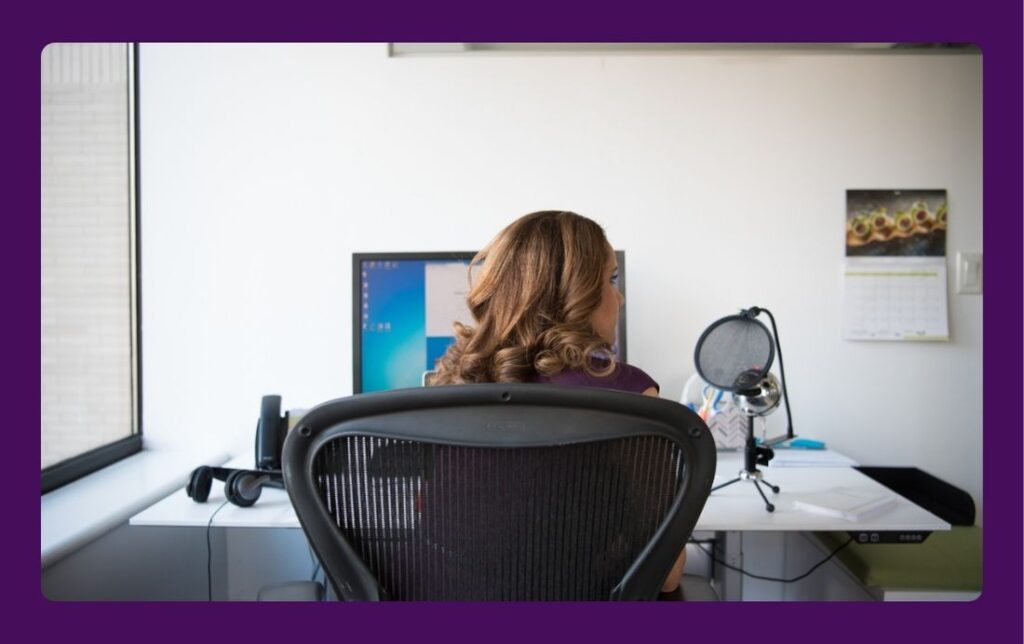 An artistic entrepreneur at her desk, blending creative work on the microphone with business tasks on the computer, a key part of the journey to business success.